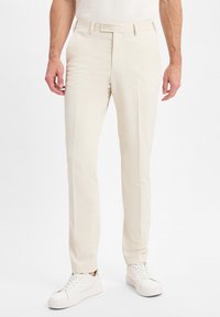 Beige maßgeschneiderte Hosen aus leichtem Stoff, mit flacher Vorderseite, Gürtelschlaufen und Seitentaschen, kombiniert mit weißen Sneakern.