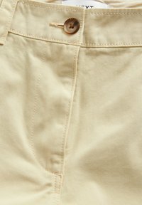 Pantalons en coton beige avec fermeture à bouton, couture proéminente et texture lisse, dotés d'un design classique à cinq poches.