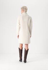 Κρέμα πλεκτό φόρεμα με φαρδύ γιακά, που διαθέτει διαμαντένιο σχέδιο και ριμπ μανσέτες, συνδυασμένο με καφέ κομψές καουμπόικες μπότες.