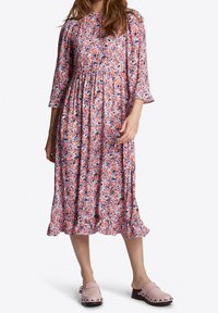 Robe midi à motifs floraux avec des manches trois-quarts. Elle présente une taille froncée, un ourlet volanté, et un mélange de motifs floraux roses, oranges et bleus.