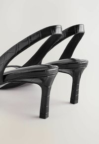 Schwarze High-Heel-Sandalen mit strukturiertem Lackfinish, die ein elegantes Slip-On-Design, breite Riemen und eine spitze Zehenpartie aufweisen.