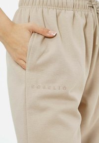 Beige Jogginghosen mit elastischem Bund und Seitentaschen, versehen mit dezent geprägtem Markenlogo "EOSILIO" auf der Vorderseite. Weicher Stoff.