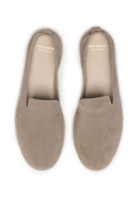 Chaussures slip-on en suède beige avec un bout arrondi et des coutures minimales. Texture lisse et semelle plate sans quincaillerie visible.