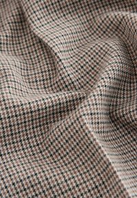 Textured fabric featuring a small houndstooth pattern in beige, brown, and black, with soft draping and a woven finish.