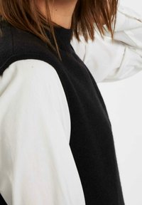Maglione nero a maglia con collo alto e corpo testurizzato di colore nero, caratterizzato da lunghe maniche bianche che contrastano nettamente con il colore del corpo.