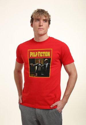 Rød bomuld t-shirt med et grafiktryk af to mænd, der holder pistol fra "Pulp Fiction", med gul og sort tekst omkring billedet.