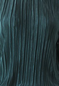Tessuto plissettato color turchese con strisce verticali, che mostra una lieve lucentezza e una texture morbida. Nessun hardware visibile o dettagli aggiuntivi.