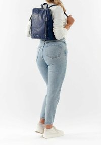 Námořnický kožený batoh s texturovaným povrchem, s dvojitými zipy a nastavitelnými popruhy, nošený s světle modrými džíny a bílými teniskami.