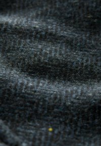 Dark woolen fabric with a textured, ribbed pattern. The surface is fuzzy, featuring a blend of dark gray and subtle blue hues.