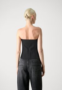 Top sans bretelles noir avec un corsage ajusté, texture lisse et coutures discrètes, associé à un jean gris taille haute avec poches arrière.
