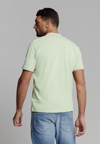 Lichtgroen polo-shirt met korte mouwen, een kraag en een rechte onderrand. Gemonteerd met blauwe spijkerbroeken, wat een eenvoudige en casual uitstraling geeft.