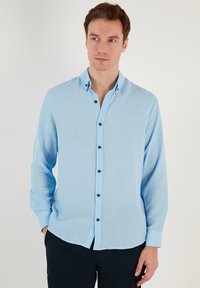 Camicia a maniche lunghe color azzurro chiaro con colletto button-down, bottoni scuri e tessuto strutturato. Presenta un taglio rilassato.