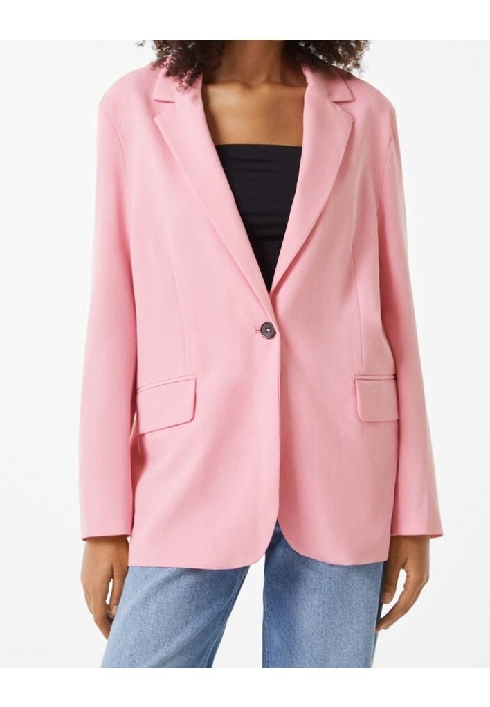 Femme portant un blazer rose à un seul bouton sur un haut noir et un jean bleu, debout, les bras détendus le long du corps.