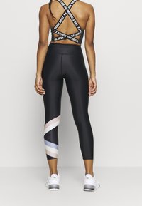 Czarne legginsy sportowe z teksturowanym wykończeniem, z ukośnym wzorem w pastelowe paski. Widok z tyłu pokazuje biustonosz sportowy z krzyżującymi się ramiączkami.