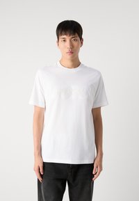Weißes T-Shirt aus Baumwolle, mit kurzen Ärmeln und Rundhalsausschnitt, mit erhabenem "BOSS"-Logo auf der Vorderseite. Glatte Textur.