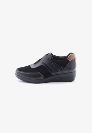 Zapato casual negro con tiras de velcro, parte superior de ante y cuero, acento marrón en el talón y suela baja tipo cuña.