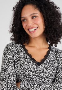 Haut à manches longues en imprimé léopard avec un décolleté en V bordé de dentelle noire. Le tissu a une texture douce avec une finition légèrement brillante.