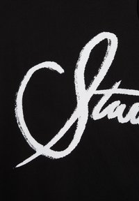 Écriture cursive blanche avec une forme de cœur à gauche, dessinée sur un fond noir, faisant partie d'un mot ou d'un dessin manuscrit plus grand.