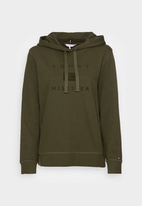 Sudadera verde oliva con capucha ajustable, puños y dobladillo acanalados. Presenta un gran texto de logo en negro "TOMMY HILFIGER" en la parte delantera.