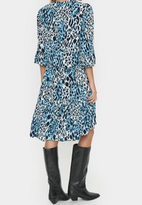 Lagermodell med djurtryck i blå och svart tyg, med trekvartslång ärm och hög halsringning. Matcha med knähöga svarta stövlar.