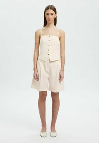 Beige ærmeløs top med fem knapper foran, parret med matchende løse shorts. Materialet ser struktureret og letvægtsagtigt ud.