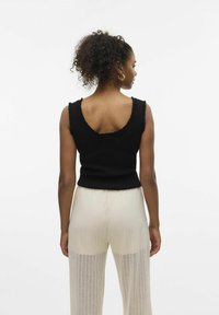 Top sin mangas negro con canalé y escote ondulado, ajustado al cuerpo, combinado con unos pantalones anchos, de pierna ancha y plisados en un color contrastante.
