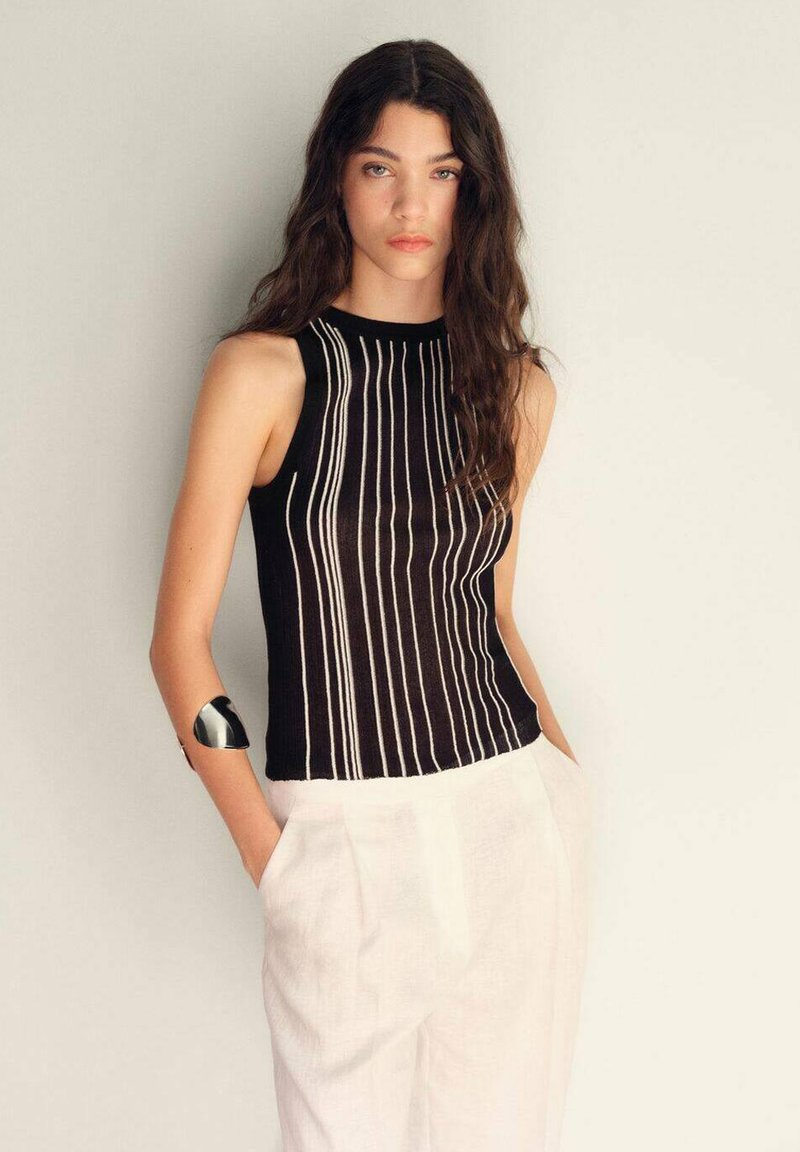 Top nero senza maniche con strisce bianche verticali, texture a costine e collo alto, abbinato a pantaloni chiari e comodi.