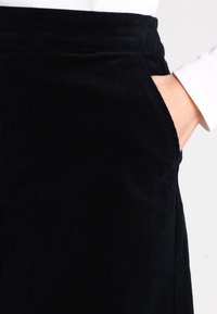 Mustat corduroy-housut, joissa on pehmeä pinta, sivutaskut ja sileä vyötärö. Kankaassa on hienoja pystysuoria urituksia.