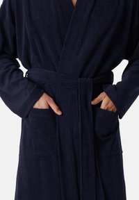 Mørkeblå badekåbe lavet af blødt, tekstureret stof. Har en talje-bånd, lange ærmer og to forlommer.