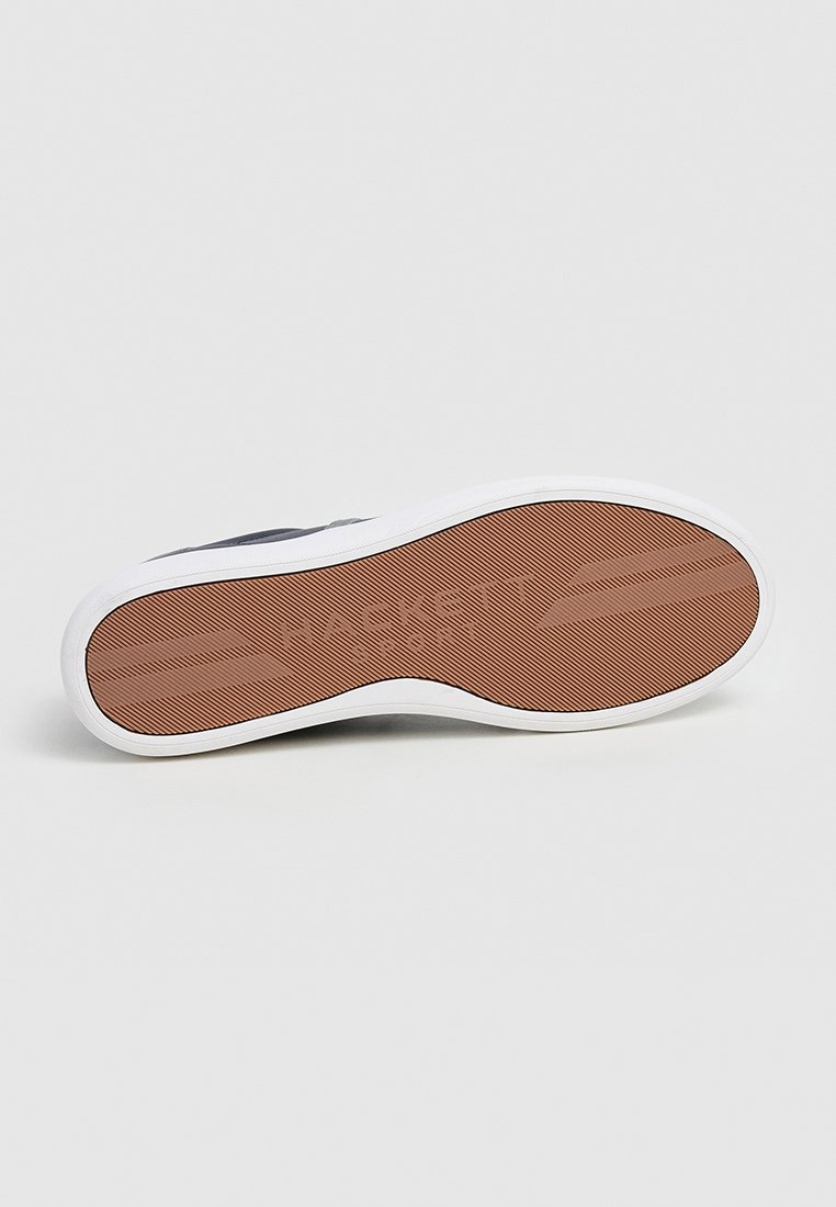 Semelle d'une basket avec une surface en caoutchouc texturé marron, un bord blanc et le logo de la marque. Conçue pour l'adhérence et la durabilité.
