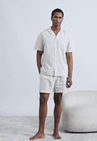 Ανοιχτό γκρι κοντομάνικο πουκάμισο και ταιριαστό σορτς με διακριτικό ριγέ μοτίβο, κατασκευασμένα από απαλό ύφασμα. Διαθέτουν μία τσέπη στο στήθος.