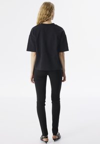 Top negro de manga corta con tejido texturizado, presenta un cuello redondo y grabados visibles, combinado con pantalones ajustados negros y sandalias de tacón.