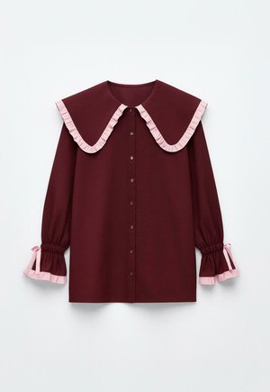 Blusa marrone con un ampio colletto arricciato, dettagli rosa, chiusura frontale con bottoni e maniche gather con volant rosa ai polsini.