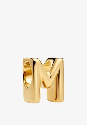Anello dorato a forma di lettera "M", con una superficie liscia e lucida, bordi arrotondati e un'apertura circolare.