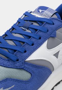 Blue athletic shoe with textured suede and smooth synthetic overlays. Features a white logo and lacing system, with a cushioned midsole.