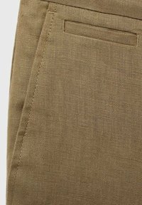 Gros plan d’un tissu en lin beige avec un tissage texturé et deux poches cousues, une horizontale et une verticale.
