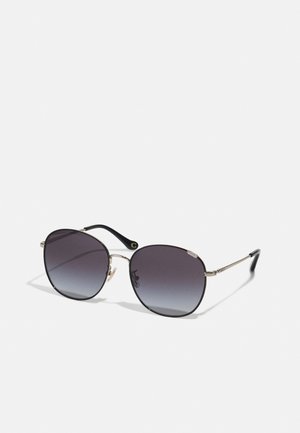 Óculos de sol com lentes ovais, armação metálica prateada, hastes pretas e lentes cinza degradê com um leve escurecimento na parte superior.