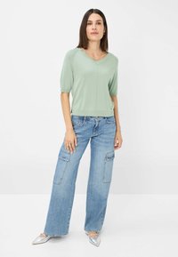 Top verde chiaro a maniche corte con scollatura a V, abbinato a pantaloni cargo in denim blu a gamba larga con tasche laterali e una finitura testurizzata.