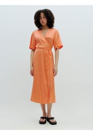 Oranje satijnen omslagjurk met korte mouwen en een strik taille. Heeft een middellange snit en een gladde, glanzende textuur. Gepaard met zwarte sandalen.