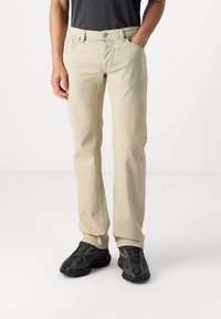 Jeans de mezclilla beiges con corte recto, cinco bolsillos y costuras en contraste. Combinados con zapatillas negras texturizadas.