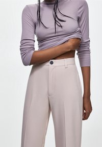Haut à manches longues côtelé couleur lavande clair et pantalon beige taille haute avec plis sur le devant et fermeture à bouton. Texture lisse et coupe ajustée.