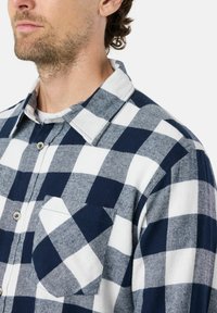 Marineblauw en wit geruite flanellen shirt met lange mouwen, knoopsluiting en een enkele borstzak. Getextureerde stof met een klassiek ruitpatroon.
