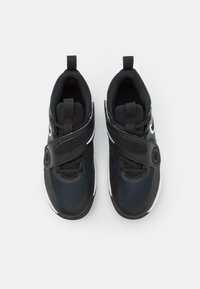Chaussures de sport noires avec empeigne en mesh, sangle Velcro et lacets. Présentent des accents blancs et une semelle texturée pour une meilleure adhérence. Vue de dessus.