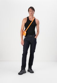 Tmavomodré denimové džínsy, čierny top bez rukávov, oranžová crossbody taška a čierne tenisky. Jednoduchý silueta a funkčné dizajnové detaily.
