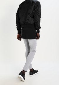 Veste bomber noire avec poignets côtelés, associée à un jean slim gris clair et des baskets noires à semelles blanches.