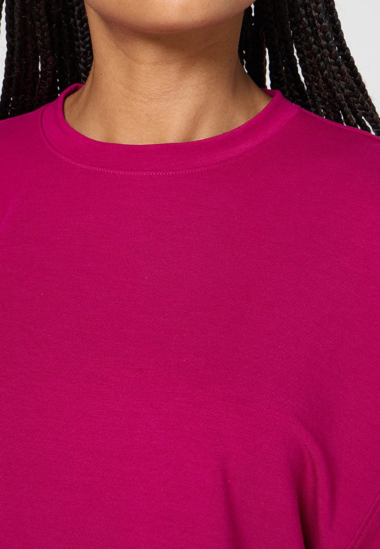Camiseta de algodón fucsia con cuello redondo y mangas cortas, que presenta una textura suave y costuras uniformes alrededor del escote.