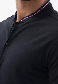 Polo shirt nera con colletto a bottoni e dettagli rossi e bianchi, tessuto testurizzato e design aderente.