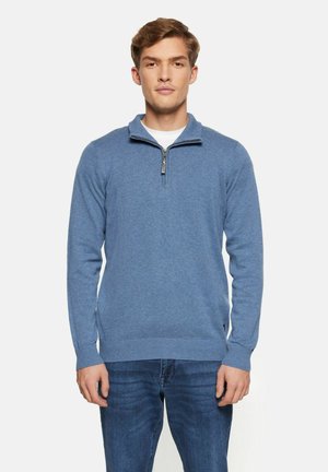 Blue knitted sweater with a zippered collar, ribbed cuffs and hem. Soft texture and fitted design, paired with blue denim jeans.