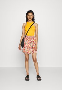 Top laranja sem mangas combinado com uma saia mini estampada em flores com várias cores. Usado com sandálias tipo slide pretas e uma bolsa pequena.
