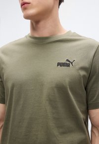 Λαδί βαμβακερό T-shirt με στρογγυλή λαιμόκοψη, με μαύρο κεντημένο λογότυπο Puma στο στήθος. Λεία υφή, κοντά μανίκια.